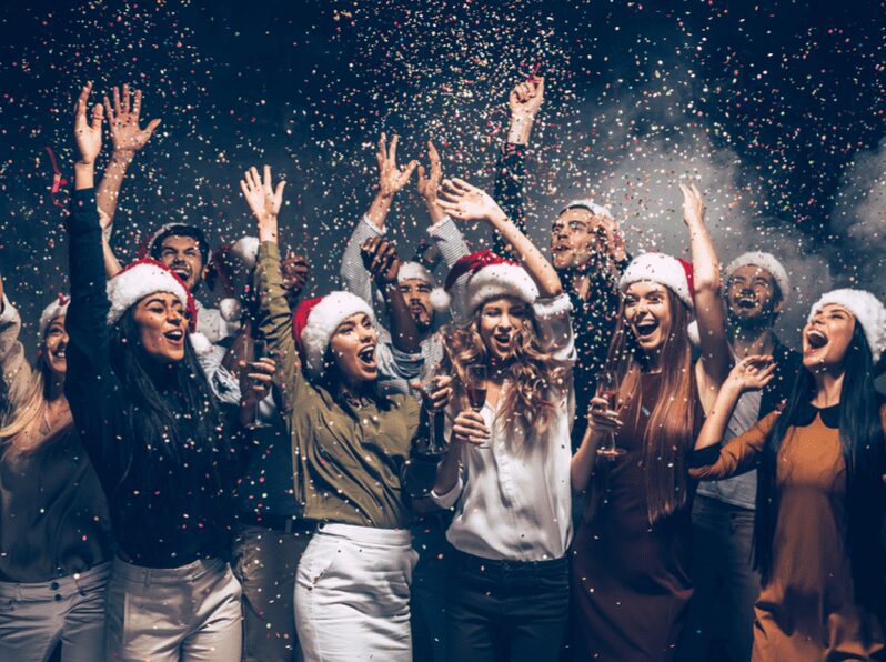 Group of beautiful young people in Santa hats throwing colorful confetti celebrating New Year together. Group of beautiful young people in Santa hats throwing colorful confetti